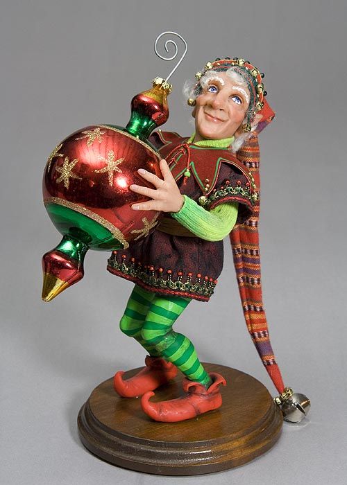 Christmas Elf dressed in red elf shoes, green striped socks and a long red hat holding a Christmas ornament. fairiehollow